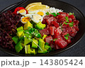 Fresh poke bowl with tuna, avocado, and vegetables served on a black plate 143805424