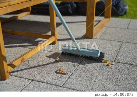Outdoor broom sweeping dry fallen leaves from patio tiles. Autumn yard cleanup Outdoor broom sweeping dry fallen leaves from patio tiles. Autumn yard cleanup 143805878
