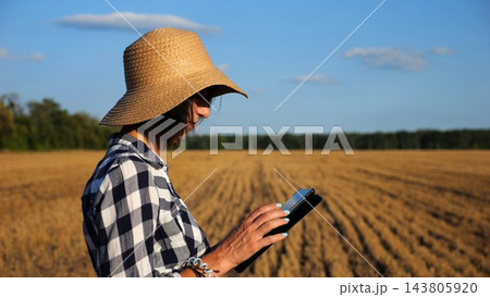 Adult farmer using digital tablet at wheat meadow on sunny day. Female agronomist monitoring harvest at barley field. Beautiful scenic landscape. Concept of agricultural business. Slow motion Adult farmer using digital tablet at wheat meadow on sunny day. Female agronomist monitoring harvest at barley field. Beautiful scenic landscape. Concept of agricultural business. Slow motion 143805920