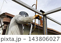 Manual laborer in protective mask weld iron detail on carport frame. Professional young repairman with welding machine working at construction. Male welder operating with metal at the site. Close up 143806027