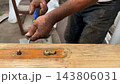 Adult male hands use a screwdriver to remove a door lock mechanism from a wooden door outdoor. Worker carefully loosens the screws and disassembles the hardware during home repair and maintenance work 143806031