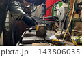Male hands in protective gloves of mechanic operate a drill press while machining a metal detail at garage. Repairman works carefully in a small workshop, concentrating on technical repair. Close up 143806035