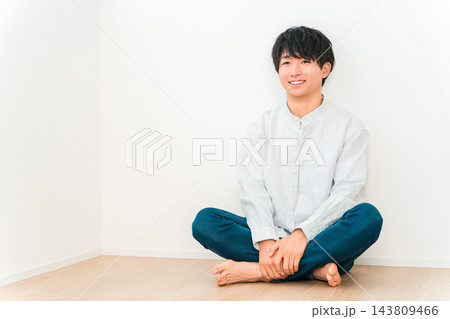 家の床にあぐらをかいて座り、爽やかな笑顔を見せる20代の若い男性。 143809466