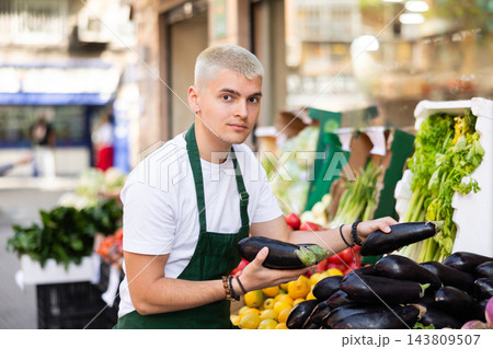 Guy shop seller puts eggplant goods on display case Guy shop seller puts eggplant goods on display case 143809507