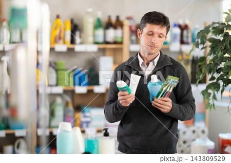 Male shopper chooses dental kit - toothbrush and toothpaste in the supermarket 143809529