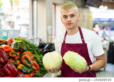 Young guy seller offers cabbage in vegetable shop 143809559