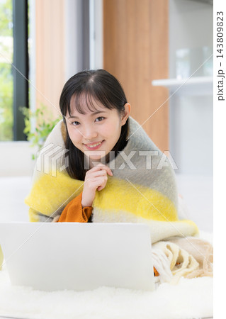 冬の自宅で暖かいストールやブランケットにくるまりながらパソコンを使う笑顔の若い日本人女性カメラ目線 冬の自宅で暖かいストールやブランケットにくるまりながらパソコンを使う笑顔の若い日本人女性カメラ目線 143809823