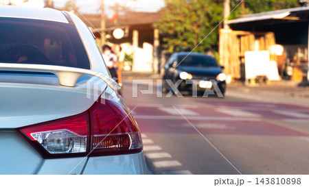 Rear view of a white car stopped on a city street during the day. Showing its detailed tail light and distant traffic on the road. Car is parked right on the red line which marks pedestrian crossing. 143810898
