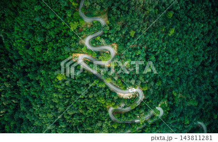 Top-down aerial view of curved road passing through lush green mountain forest 143811281
