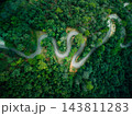 Top view aerial drone shot of winding road through dense green forest 143811283