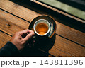 Hand holding a ceramic cup of hot espresso with perfect crema over a wooden table 143811396