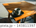 Hot espresso in a rustic ceramic cup on a wooden table with morning sunlight and hard shadows 143811397