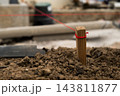A wooden stake secured with red string stands in soil, indicating layout on a construction site. A closeup of the marked stake among dirt and construction materials. 143811877