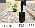 White decorative pebbles create a border along a garden path. A black hand trowel stands upright among the pebbles, complementing the landscaping design. 143811878
