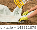 Freshly turned soil lines a trench as protective fabric is spread out for drainage system installation. Visible yellow hoses and tools indicate an active construction site focused on water management. 143811879