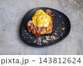 Croissant sandwich with scrambled eggs and crispy bacon on a black plate 143812624