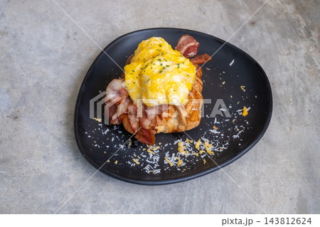 Croissant sandwich with scrambled eggs and crispy bacon on a black plate Croissant sandwich with scrambled eggs and crispy bacon on a black plate 143812624