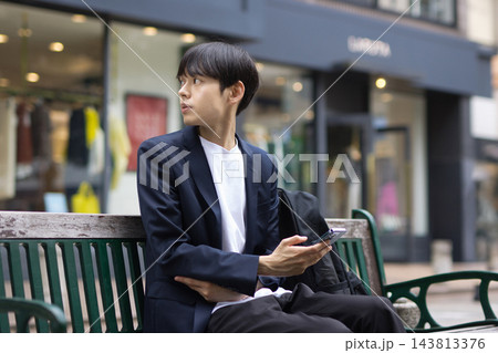 ベンチに座ってスマホを見る20代男性のビジネスマン ベンチに座ってスマホを見る20代男性のビジネスマン 143813376