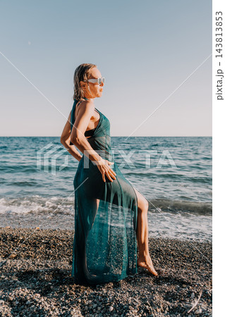 Graceful mature woman posing in a sheer green dress by the sparkling sea shore Graceful mature woman posing in a sheer green dress by the sparkling sea shore 143813853