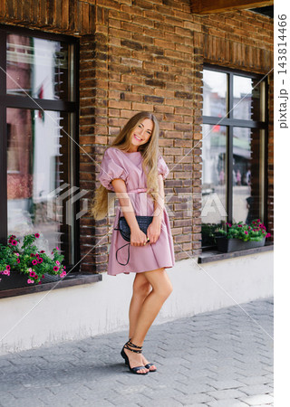 Happy woman in pink dress with mini bag by brick wall, summer city street Happy woman in pink dress with mini bag by brick wall, summer city street 143814466
