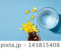 Omega 3. Yellow fish oil capsules scatter from a brown bottle next to a glass of water. 143815408