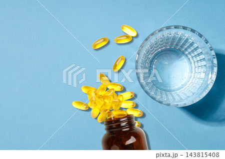 Omega 3. Yellow fish oil capsules scatter from a brown bottle next to a glass of water. Omega 3. Yellow fish oil capsules scatter from a brown bottle next to a glass of water. 143815408