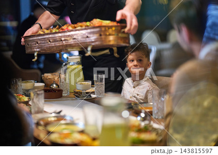 Family Dinner in Restaurant With Young Boy Watching Waiter Serve a Large Platter 143815597