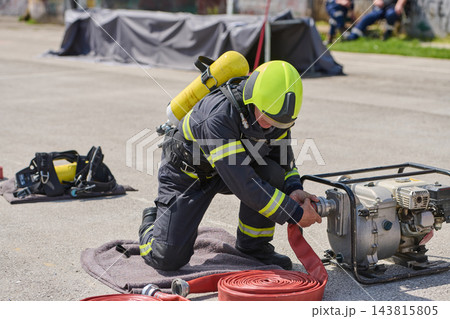 Firefighter Connecting Hose to Portable Water Pump During Outdoor Training Exercise in Protective Gear 143815805