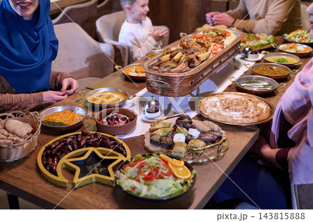 Muslim Family Sharing Iftar Meal Together At Dining Table With Middle Eastern Feast Muslim Family Sharing Iftar Meal Together At Dining Table With Middle Eastern Feast 143815888