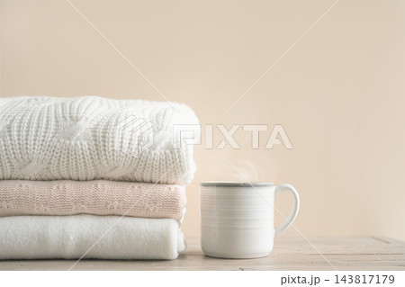 Stack of folded knitted sweaters with cup of coffee Stack of folded knitted sweaters with cup of coffee 143817179