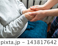 Caregiver holding elderly person's hands in comforting support and compassion at home 143817642