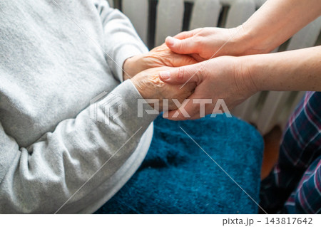 Caregiver holding elderly person's hands in comforting support and compassion at home Caregiver holding elderly person's hands in comforting support and compassion at home 143817642