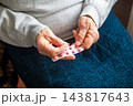 Senior holding a blister pack of pink pills in hand at home, representing medication and elderly care 143817643