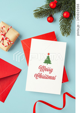 Christmas greeting card on red envelop with gift box, red ribbon and pine branch xmas ornament on blue background Christmas greeting card on red envelop with gift box, red ribbon and pine branch xmas ornament on blue background 143819168