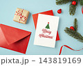 Merry christmas text on white card with red envelop, gift box, red ribbon and pine branch xmas ornament on blue background 143819169
