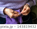 Senior hands knitting purple sweater with yarn and needle, quiet hobby and cozy home craft 143819432