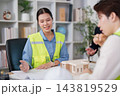 Construction project team discusses plans beside building model 143819529