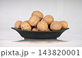 Pile of whole unshelled walnuts served on a black ceramic dish isolated against a white background 143820001