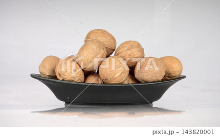 Pile of whole unshelled walnuts served on a black ceramic dish isolated against a white background 143820001