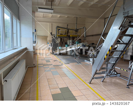 Inclined metal conveyors and tubular feeding equipment stand inside a food processing factory, illustrating industrial product handling and transfer 143820167