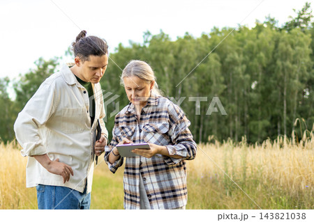 Two diverse agronomists working together with a digital tablet in a mature wheat field. Concept of smart farming, mentorship and family agricultural business. Two diverse agronomists working together with a digital tablet in a mature wheat field. Concept of smart farming, mentorship and family agricultural business. 143821038