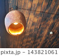 A pendant light with a warm glow and a textured terracotta shade, mounted beneath a ceiling made of wooden planks. 143821061
