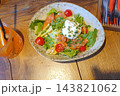 A fresh, healthy salad with salmon, romaine lettuce, cherry tomatoes, cream cheese, and chives in a rustic-style ceramic bowl on a wooden table served with an orange cocktail. 143821062