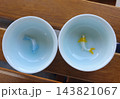 Two white porcelain tea cups with blue glaze and 3D ceramic koi fish figurines inside, one blue and one yellow, seen from above on a wooden table 143821067