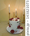 White buttercream birthday cake decorated with red piped roses and green vines, golden wavy candles on top and lit candlesticks in brass holders 143821073