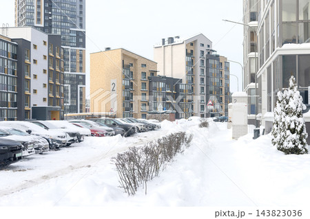 Residential courtyard with parked cars covered in winter snow near apartment buildings. Modern high rise condominium facade, snowdrift parking lot. Multistory architecture, balcony windows. Residential courtyard with parked cars covered in winter snow near apartment buildings. Modern high rise condominium facade, snowdrift parking lot. Multistory architecture, balcony windows. 143823036