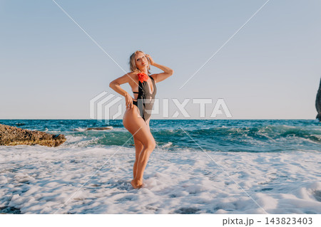 Coastal vacation getaway featuring mature woman posing gracefully in black swimwear by ocean surf during sunset Coastal vacation getaway featuring mature woman posing gracefully in black swimwear by ocean surf during sunset 143823403