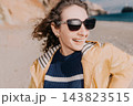Woman beach vacation smiling young woman in yellow jacket and sunglasses enjoying a windy day at the seaside during her spring vacation 143823515