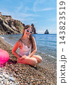 Beach woman summer happy young woman sits on a pebble shore near the turquoise sea during a sunny coastal vacation 143823519