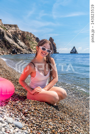 Beach woman summer happy young woman sits on a pebble shore near the turquoise sea during a sunny coastal vacation Beach woman summer happy young woman sits on a pebble shore near the turquoise sea during a sunny coastal vacation 143823519